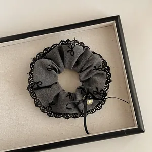 Detail von dunkelgrauem Scrunchie mit Spitzenkante, Schleifenstickerei und Anhänger