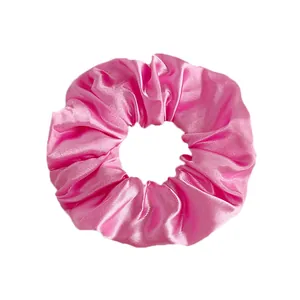 Detailed view of large bright pink satin scrunchie showing glossy fabric and natural folds