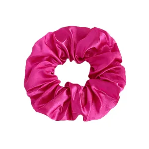 Detailed view of fuchsia satin scrunchie showing glossy silk texture and pleated design