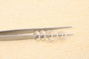 Set of 6 graduated S925 silver earring hoops held by tweezers on orange background