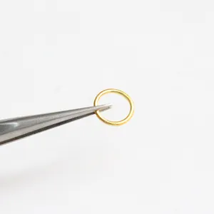 Macro shot of a tiny gold-plated jump ring held by tweezers for jewelry making