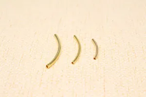 Macro shot of three lengths of curved hollow tube beads in polished gold finish