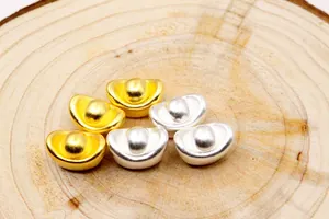 Nahaufnahme von 3D-Gold- und Silber-Yuan Bao-Charms für DIY-Schmuck auf Holzoberfläche