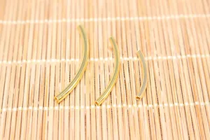 Three sizes of curved golden hollow tubes for DIY jewelry making on a bamboo mat