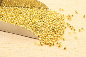 Detailed close-up of golden metal beads pouring from a scoop for DIY jewelry making