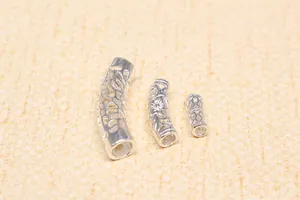 Macro detail of three hollow S925 sterling silver curved tube beads with floral cutout patterns