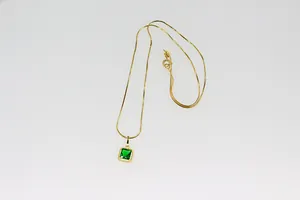 Detalle de colgante de gema verde cuadrada con cadena de serpiente dorada