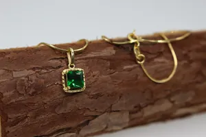 Detalle del colgante de piedra verde cuadrada con cadena dorada sobre madera