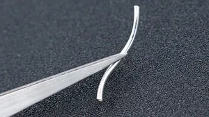 Macro shot of S-shaped 925 sterling silver tube bead held by tweezers for DIY jewelry