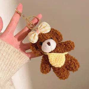 Détail d'un porte-clés ours en peluche marron foncé avec un bavoir tricoté jaune doux