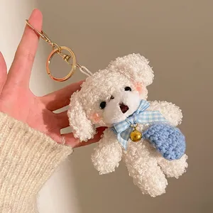 Détail du porte-clés chien en peluche blanc avec nœud bleu et petit sac tricoté