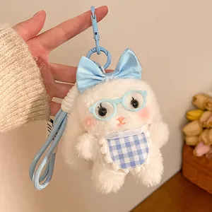 Close-up of white plush bunny keychain with blue bow, glasses, and woven strap accessory
