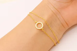 Détail d'un bracelet double chaîne doré orné d'un pendentif rond serti de zircons pavés