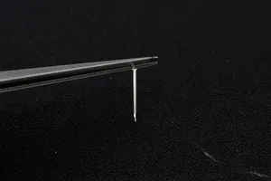Macro shot of silver rectangular stud earring components held by precision tweezers