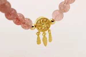 Macro-opname van S925 dromenvangerbedeltje met gouden veren op roze kristallen kralen