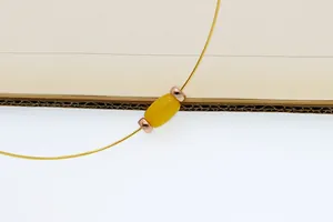 Vue macro d'un collier doré minimaliste avec une perle tonneau jaune et des perles d'espacement