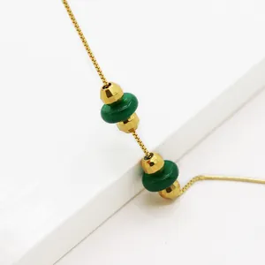 Dettaglio di una collana a catena box dorata con dischi di pietra verde e perline sfaccettate