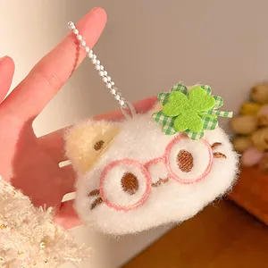 Close-up of white plush cat keychain with green clover and pink glasses held in hand