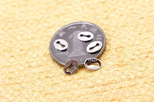 Macro shot of oval S925 sterling silver jewelry tags with Italy hallmark next to a coin