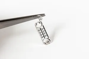 Gros plan d'un pendentif boulier en argent vieilli tenu par une pince de précision