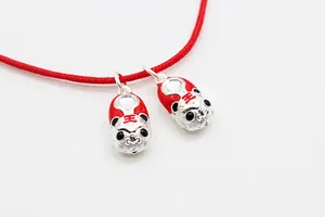 Macro shot of S925 silver tiger pendants with red enamel detailing on a red woven cord