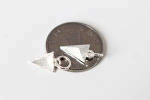 Vue macro de pendentifs triangles en argent 925 mat à côté d'une pièce pour la taille