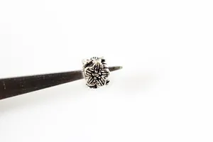 Macro detail of vintage S925 silver floral cube spacer bead held by metal tweezers