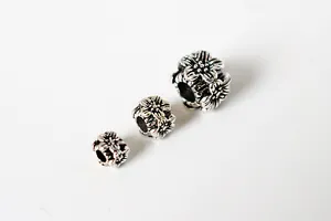Macro detail of three vintage S925 silver flower beads with oxidized floral engravings