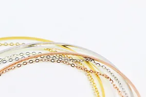 Makroaufnahme von Armreifen in Silber Gold und Roségold mit feinem Kettendetail