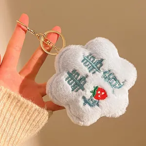 Close-up of light blue plush flower keychain with strawberry embroidery and gold hardware