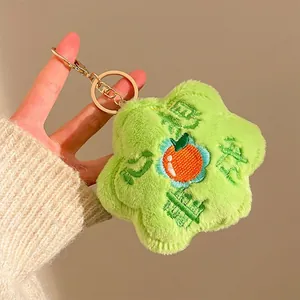 Detail of light green plush flower keychain with orange persimmon embroidery and gold clip