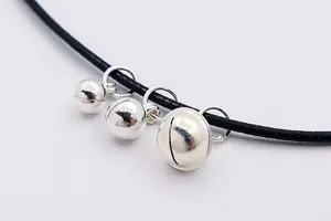Detail of three silver bell charms with metallic reflection on a black cord necklace
