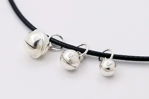 Detailed macro view of three sizes of polished silver bell pendants on a black cord