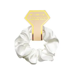 Close-up of a white satin scrunchie on a premium diamond card with gold foil edges