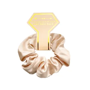 Close-up of champagne satin scrunchie on elegant display card with gold trim details