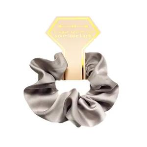 Detail view of silver grey satin silk scrunchie on decorative hexagonal paper card
