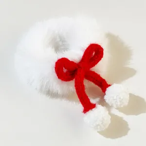 Close-up of white plush scrunchie with red knitted bow and small festive pom-poms