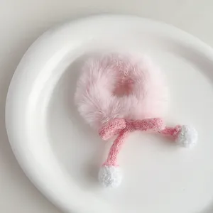 Close-up of pink plush hair tie with knitted bow and white pom-poms on a white plate
