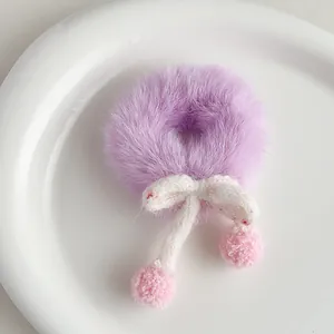 Detail of purple plush hair scrunchie with white knit bow and soft pink pom poms