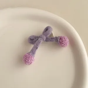 Détail d'une barrette à cheveux en tricot violet en forme de nœud avec pompons doux