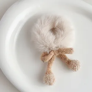 Close-up of soft plush hair scrunchie with knitted bow and pompom on ceramic plate