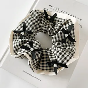 Détail du chouchou vichy avec bordure en dentelle, nœuds noirs et perles sur livre