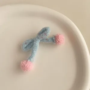 Détail d'une barrette nœud en tricot bleu clair avec des pompons roses sur un plateau