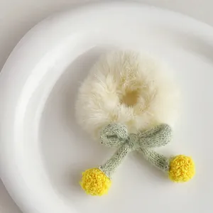 Close-up of cream plush hair tie with green bow and yellow pom-poms on ceramic plate