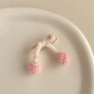 Détail d'une barrette à nœud en tricot rose avec pompons sur un plat en porcelaine