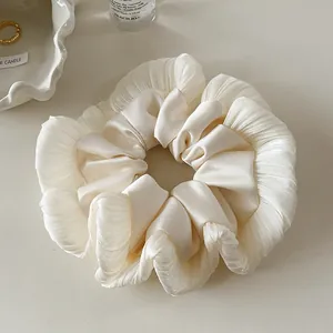 Close-up of ivory pleated silk scrunchie on a decorative ceramic tray with golden ring