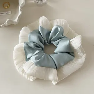 Detailed close-up of blue satin and white pleated lace hair scrunchie on an elegant setup