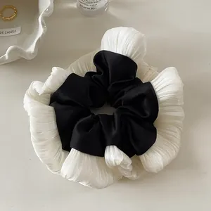 Detail of elegant black satin scrunchie with pleated white lace trim on a minimalist table