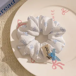 Close-up of white scrunchie with blue bows, lace trim and handmade tag on a ceramic tray