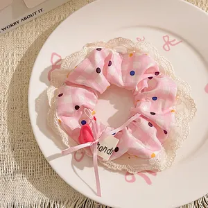 Close-up of a pink plaid scrunchie with lace trim and colorful polka dots detail.